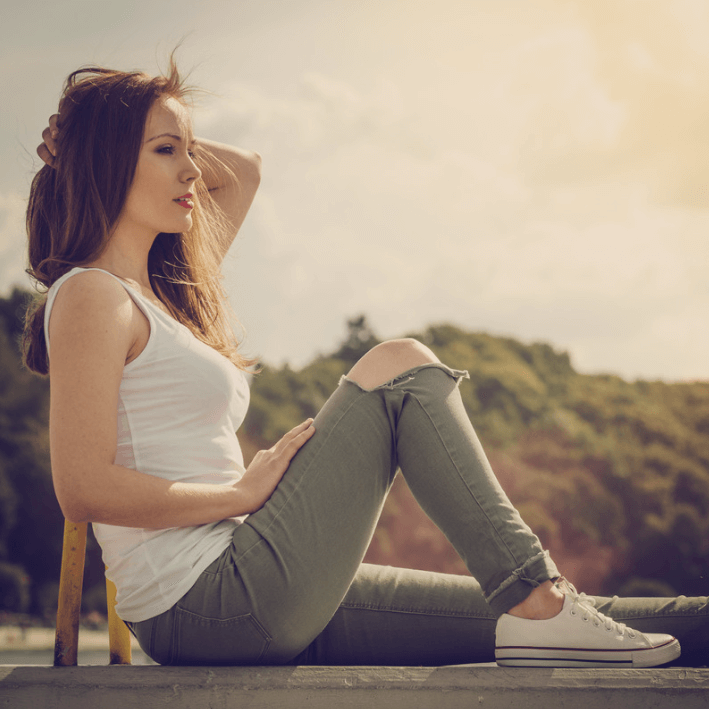 Woman sitting outdoors in casual attire, enjoying the sunlight with a serene expression.