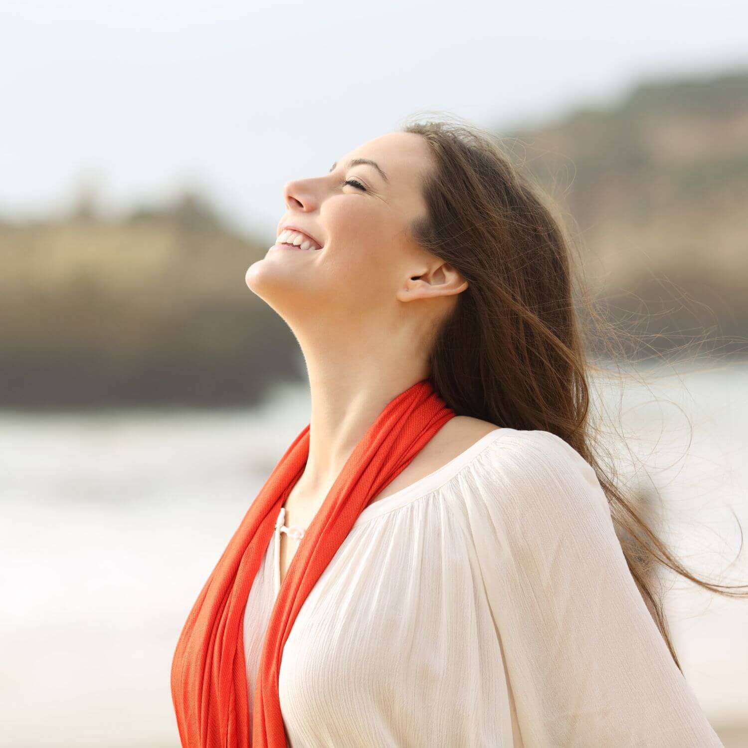 Woman smiling with a red scarf against a beach backdrop, radiating freshness and joy.