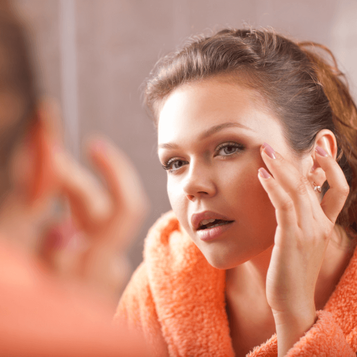 Woman applying Luxe Eye Balm in front of a mirror, showcasing her skincare routine with a radiant appearance.