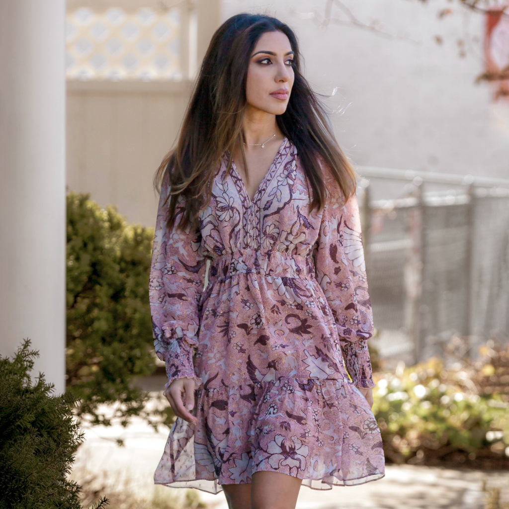 Woman wearing a floral pink dress, walking outdoors with natural light in the background.