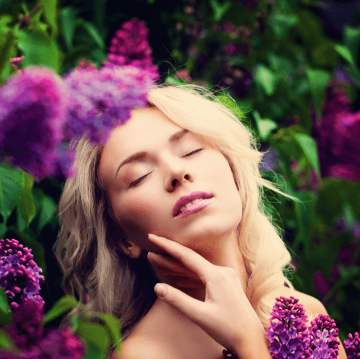 Woman with closed eyes surrounded by lilac flowers, representing beauty and skincare essence.