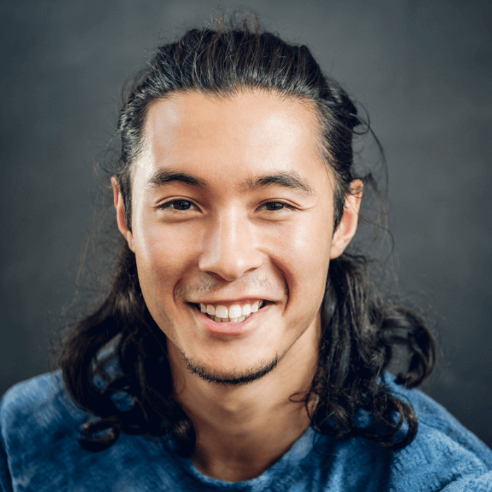 Smiling man with long hair wearing a blue shirt, representing relaxation and self-care with Vital Active Patch.