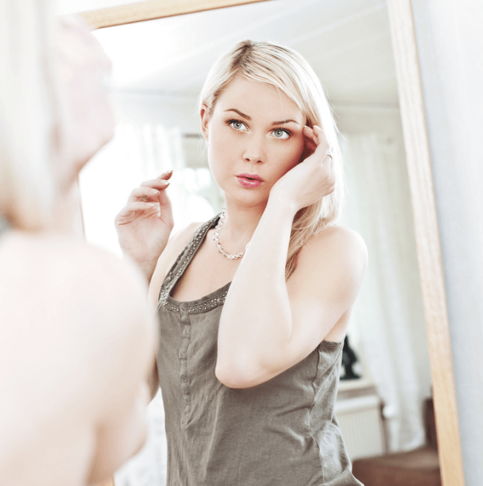 Woman applying Skin Care Spray, looking in the mirror with a refreshed expression, highlighting her radiant skin.