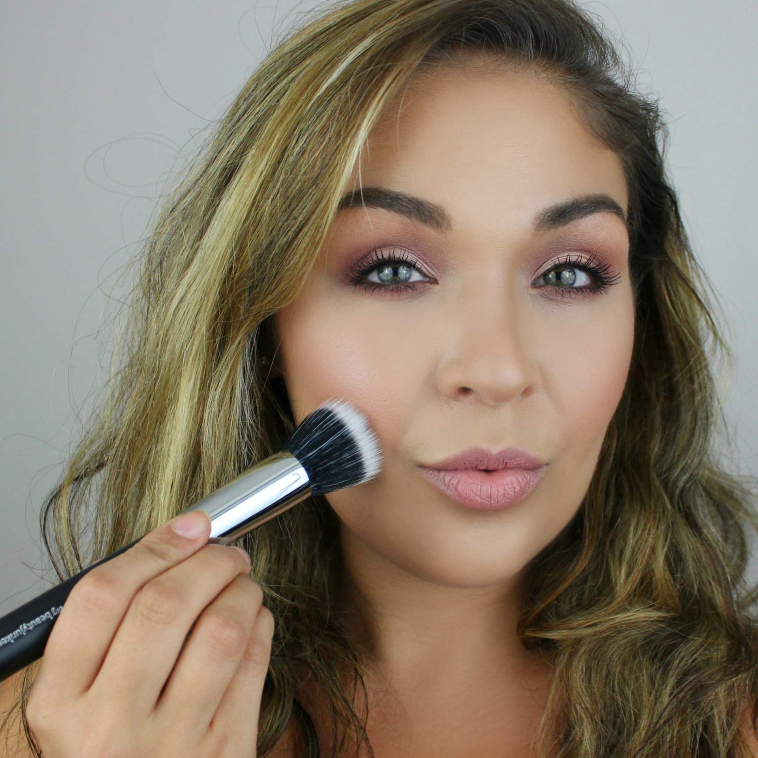 Model applying makeup with Duo Fiber Stippling Brush, featuring a soft flat-top design for smooth application.