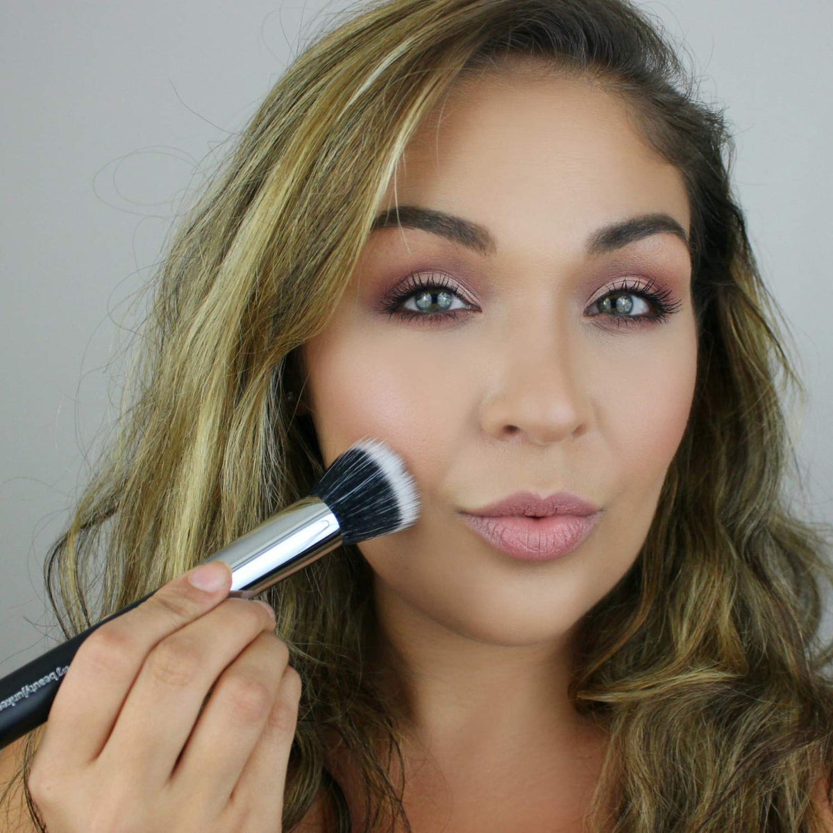 Model applying makeup with Duo Fiber Stippling Brush, featuring a soft flat-top design for smooth application.