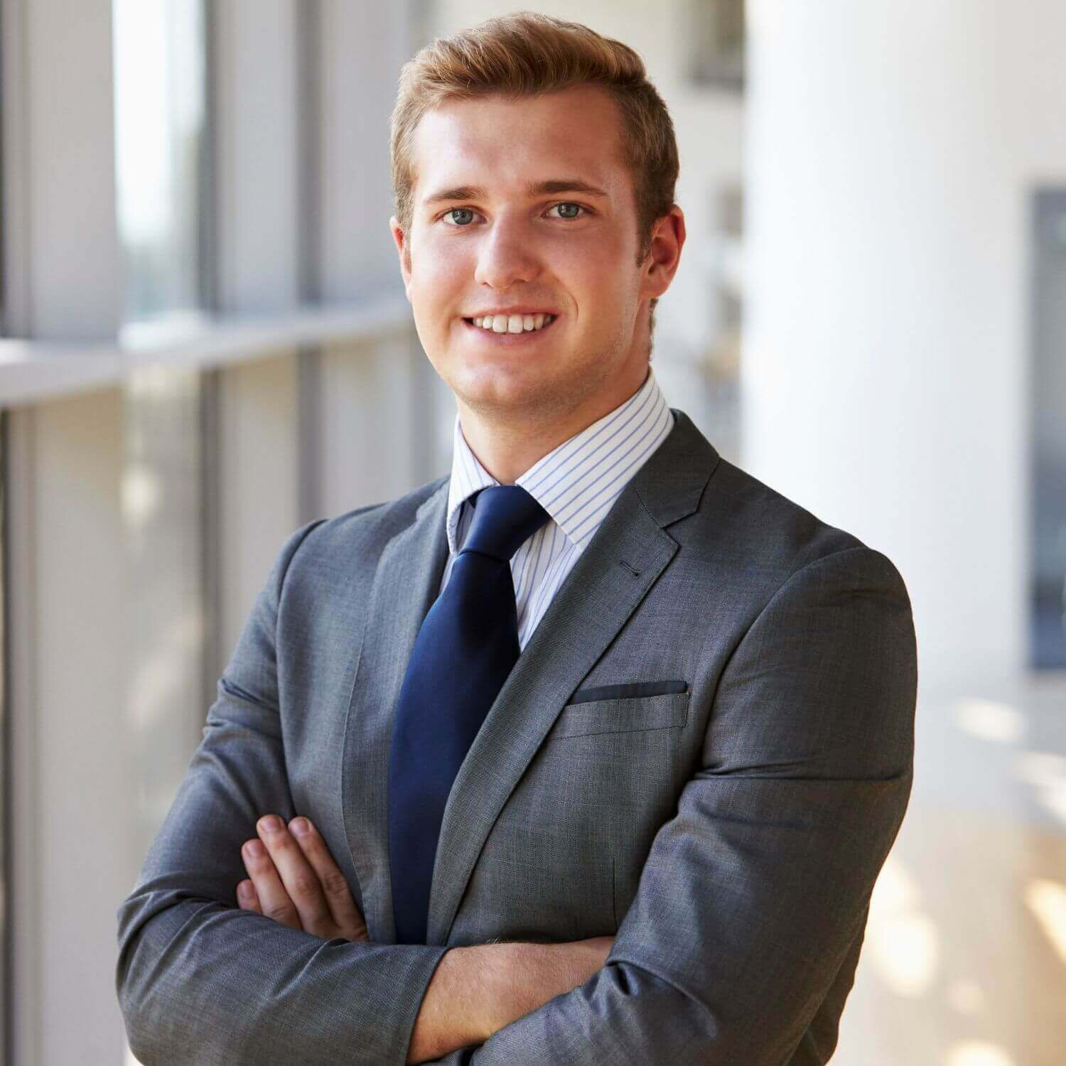 Confident young man in a suit smiling in a modern office setting.